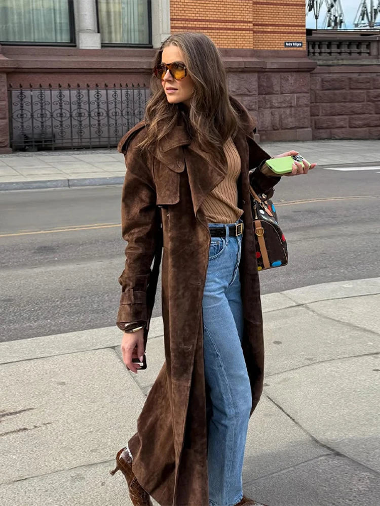 Woman wearing a brown coat and sunglasses on a city street.
