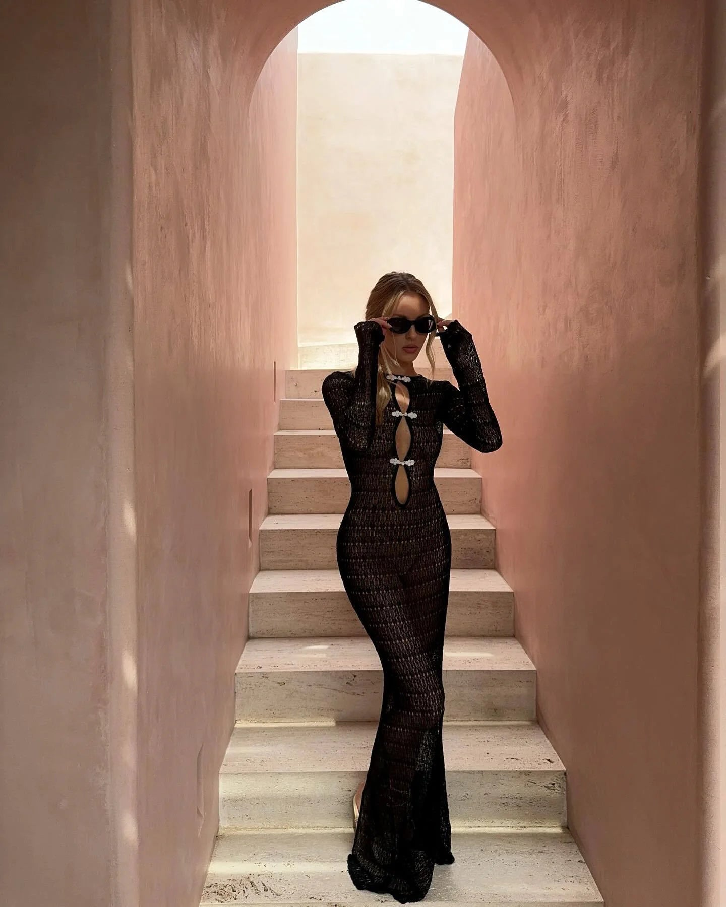 Woman in a black dress standing on a staircase with pink walls