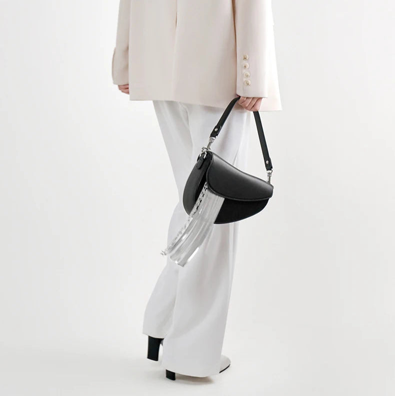 Person holding a black handbag with tassels against a white background