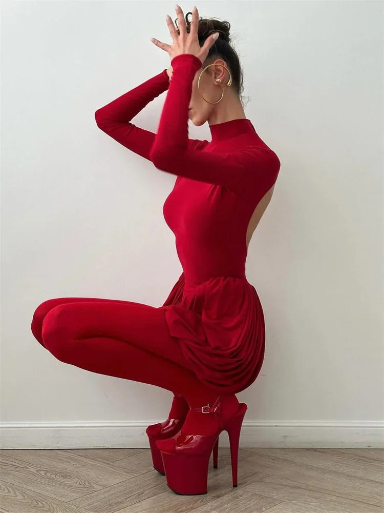 Person wearing a red dress and high heels posing against a white wall.