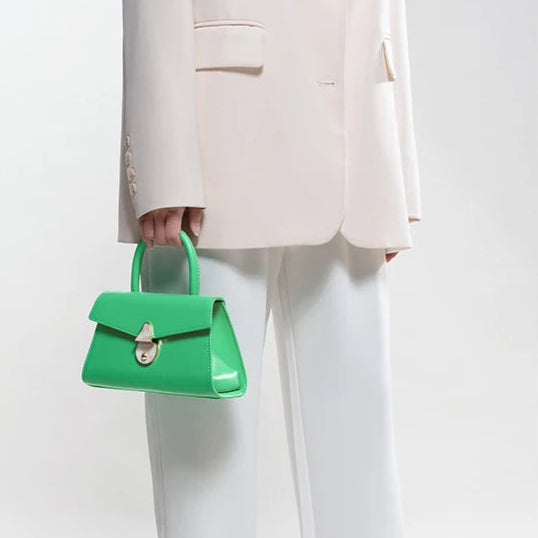 Person wearing a light pink blazer and white pants, holding a green handbag on a white background