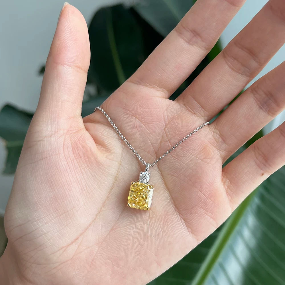 Hand holding a necklace with a yellow diamond pendant against a blurred green background