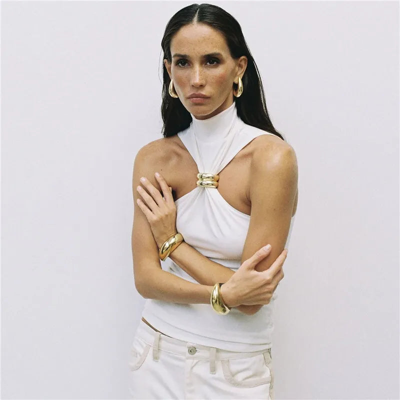 Woman wearing a white top with gold accents and gold bracelets on a plain background
