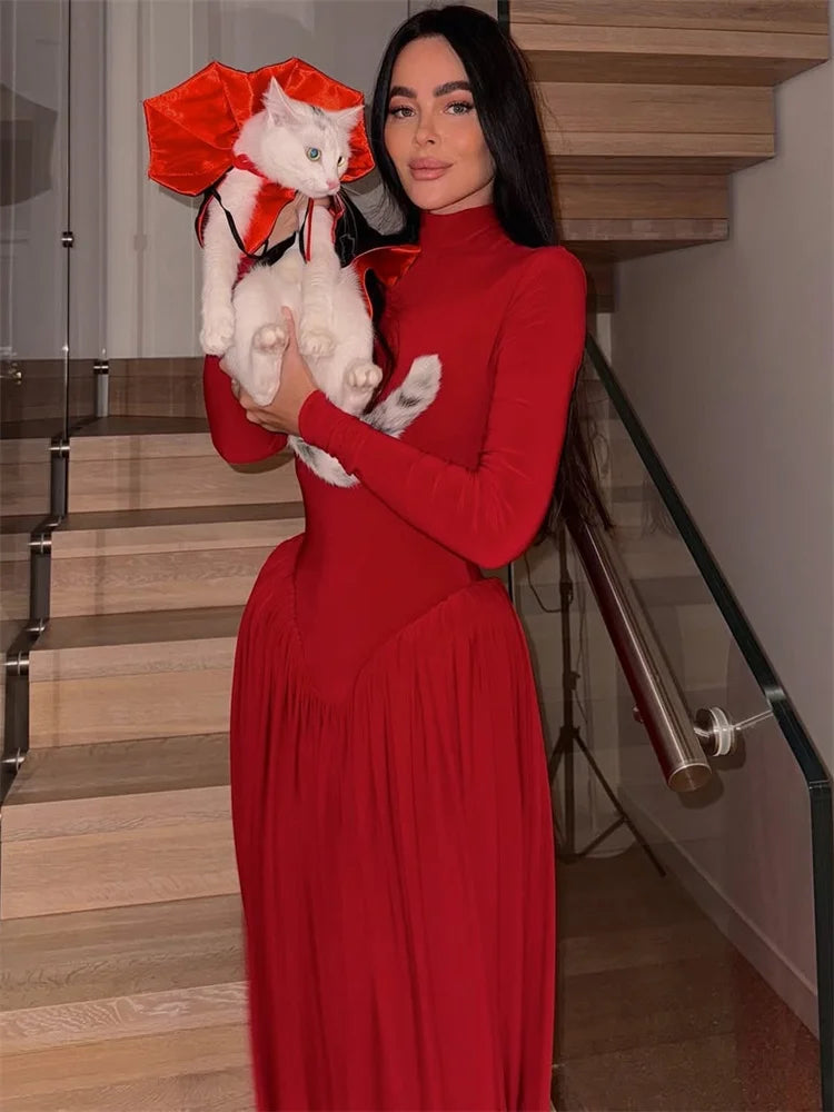 Woman in a red dress holding a white cat with a red bow, standing on a staircase.