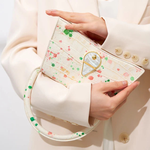 Person holding a small, decorative clutch bag with a heart design on a plain background