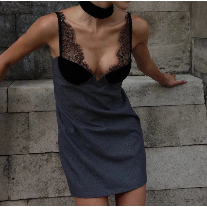 Person wearing a gray dress with black lace details against a stone wall.